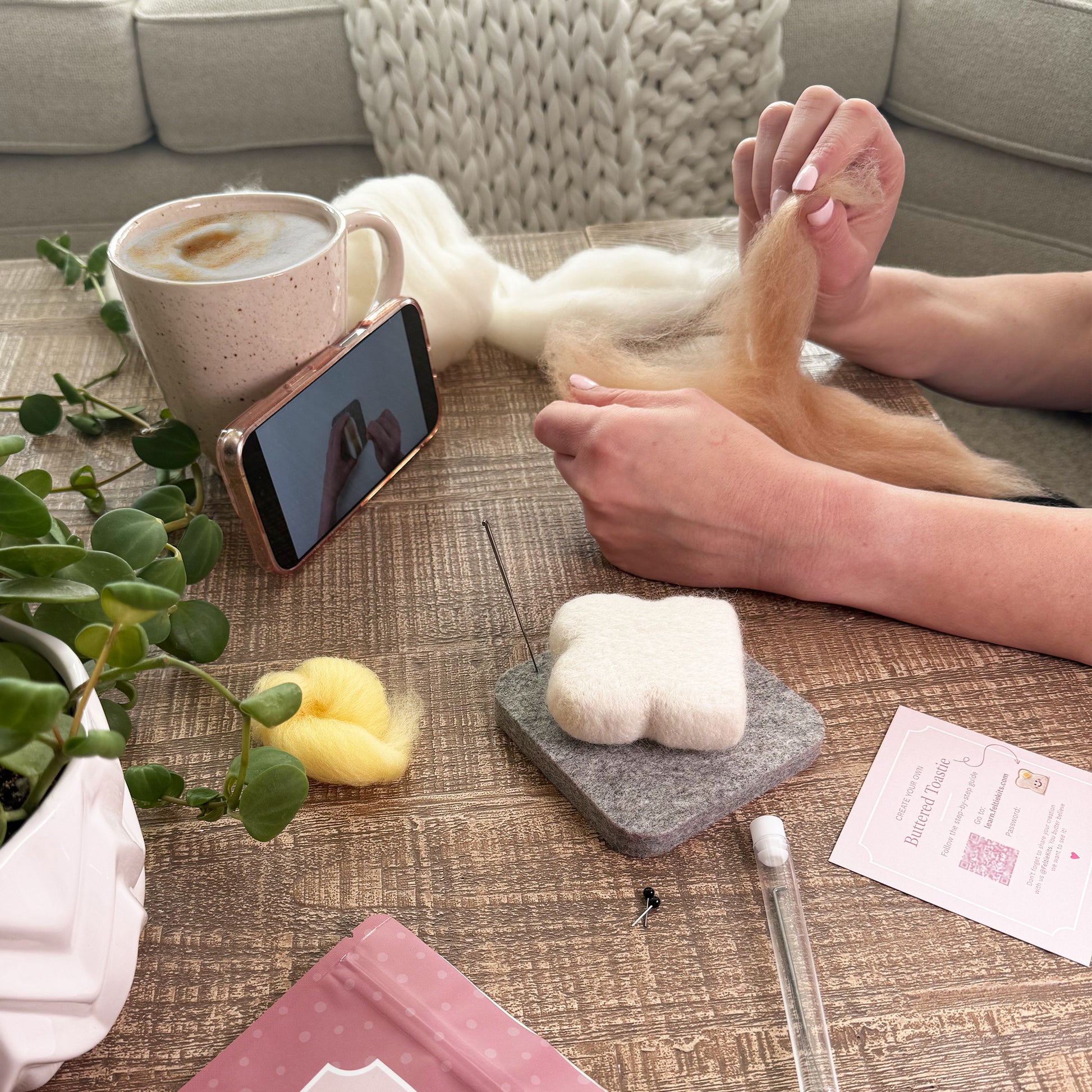 Needle felting the Buttered Toastie Feltie using the Feltie Kits tutorial, with wool, needles, tools, and a phone showing the video on a cozy workspace.