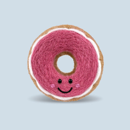Finished Pink Glazed Donut Feltie made from the Feltie Kits needle felting kit, showing the donut with pink wool, white glaze and smile. 
