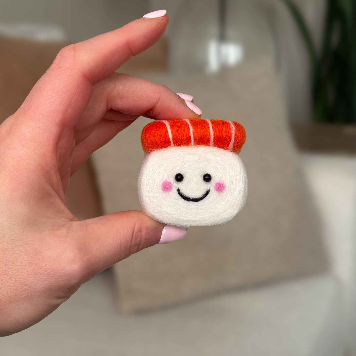 Hand holding the finished Salmon Sushi Feltie from the Feltie Kits needle felting kit, showing the white rice body and bright orange salmon top.