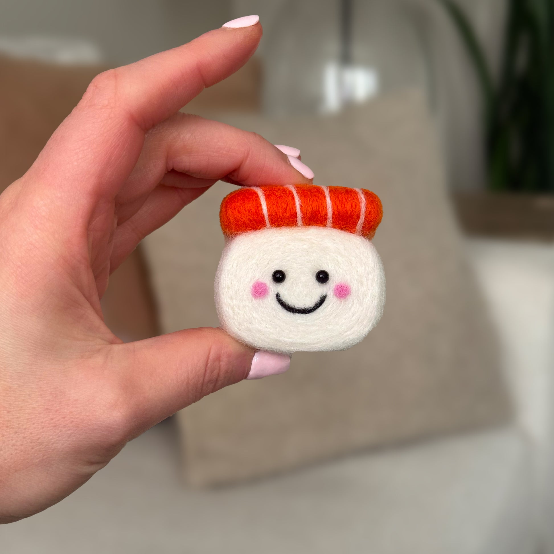 Hand holding the finished Salmon Sushi Feltie from the Feltie Kits needle felting kit, showing the white rice body and bright orange salmon top.
