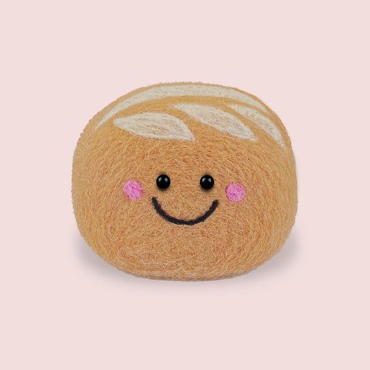 Finished Sourdough Feltie from Feltie Kits, showing a smiling felt sourdough loaf with soft tan wool texture, white scored dough details, and embroidered facial features.