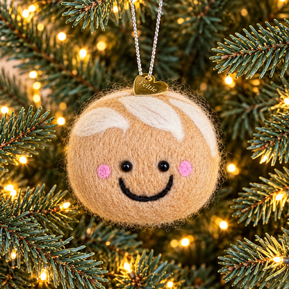 A handmade needle felted sourdough Christmas ornament hanging on a Christmas tree, with a gold heart Feltie charm and silver hanging string.